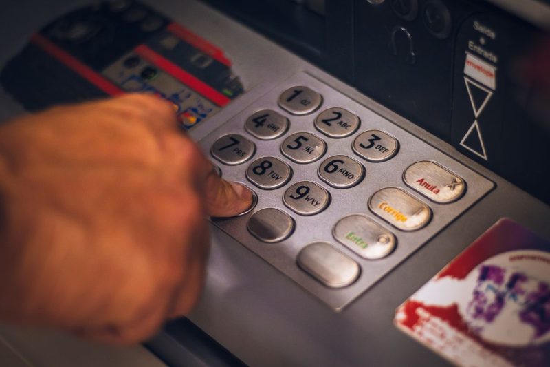 Hand at an ATM keypad, checking for withdrawal fees before confirming
